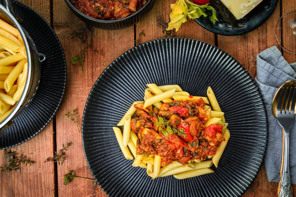 Delicious Italian pasta with hearty tomato sauce served on a dark plate, styled as a flat lay.