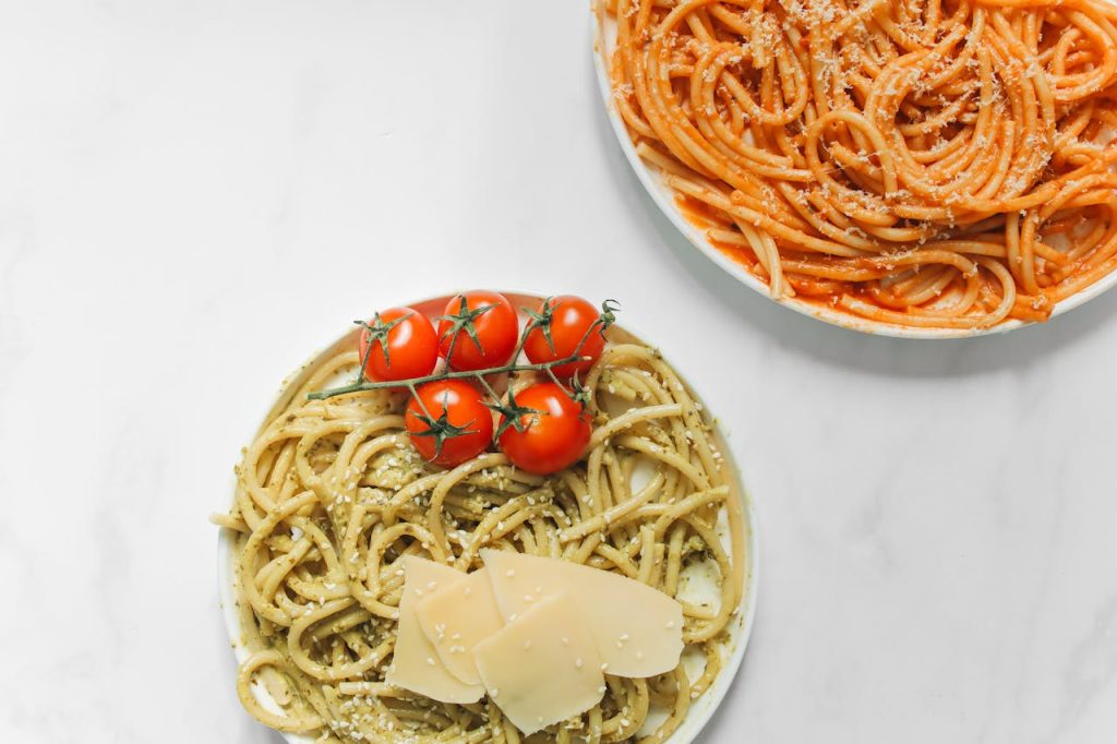 Close-up of pesto and tomato sauce pasta dishes, garnished with fresh cherry tomatoes and cheese.