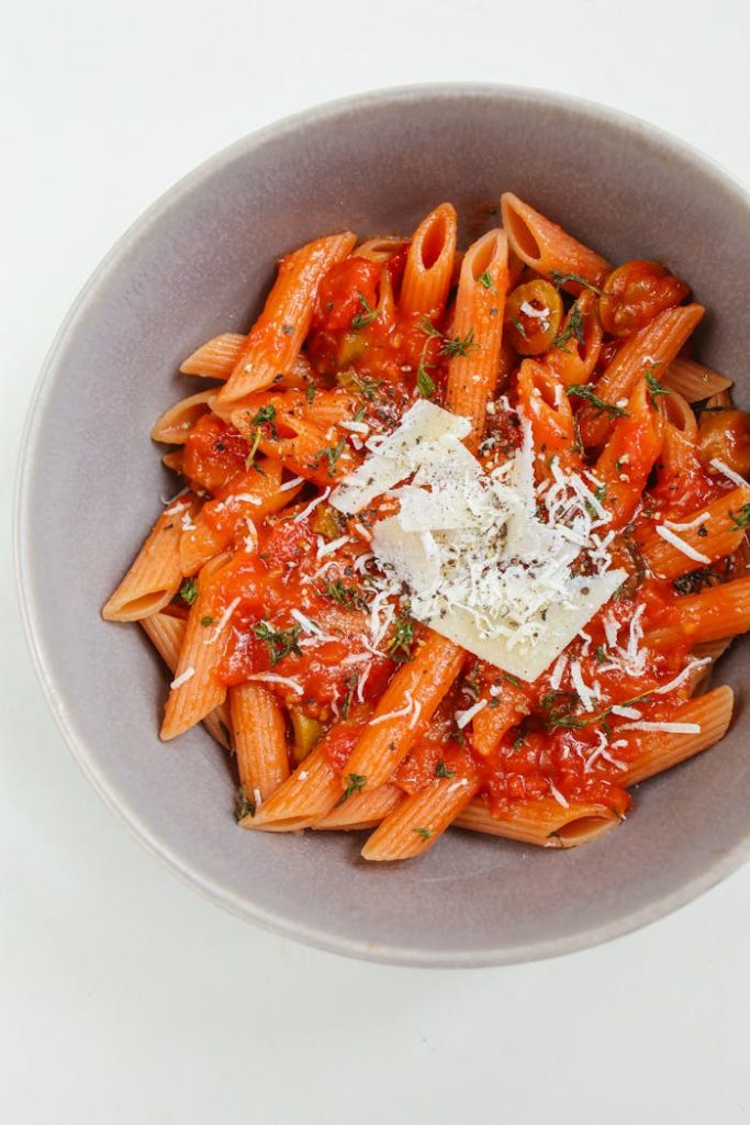 Close-up of penne pasta in red tomato sauce topped with cheese, showcasing classic Italian cuisine.