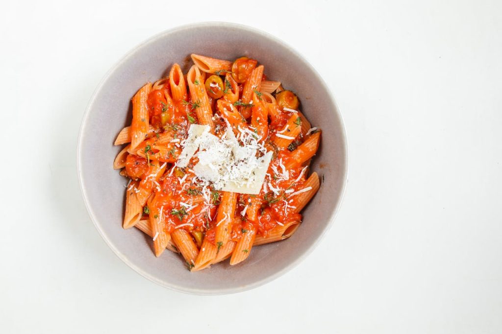 Top view of penne pasta with rich tomato sauce and grated cheese in a bowl.