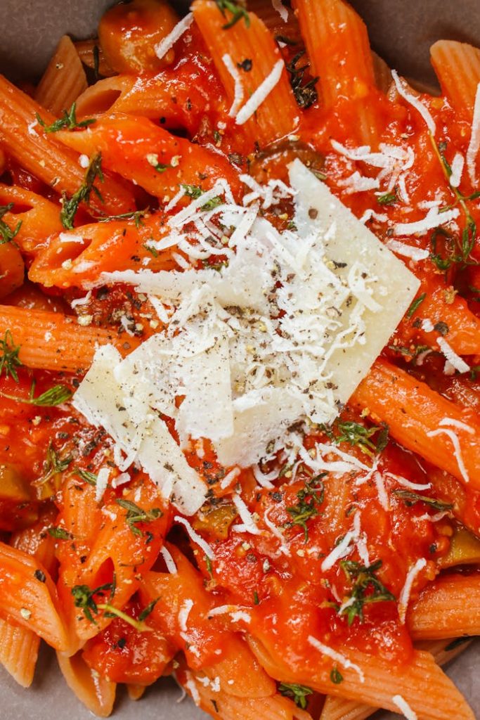 Close-up of penne pasta topped with tomato sauce, grated cheese, and herbs for a delicious Italian meal.