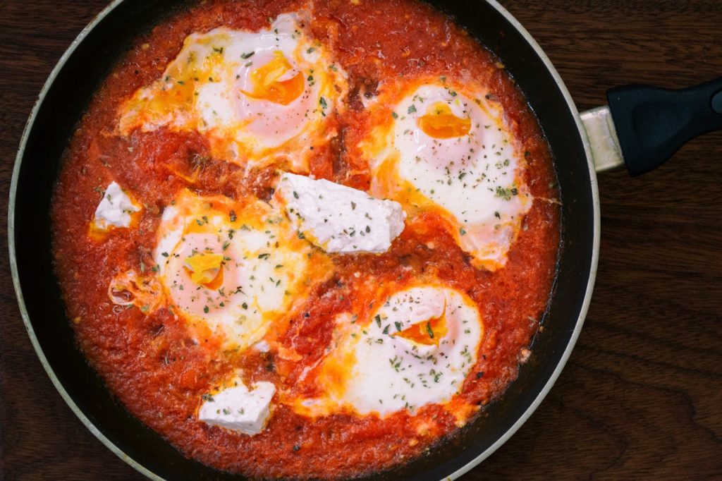 Top view of homemade shakshuka with eggs and herbs in a frying pan.